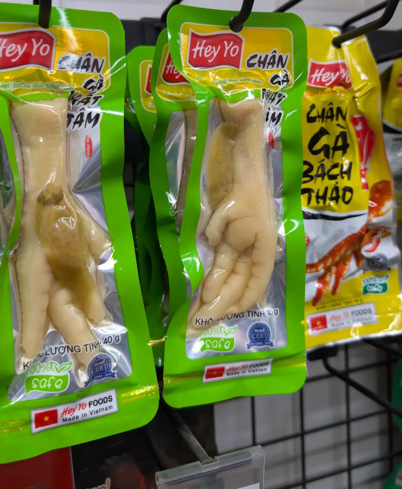 Brightly coloured vacuum-sealed snack packets hanging on a shop rack, each containing a single marinated chicken foot, labelled Chân Gà, with a price tag reading 16,000 VND.